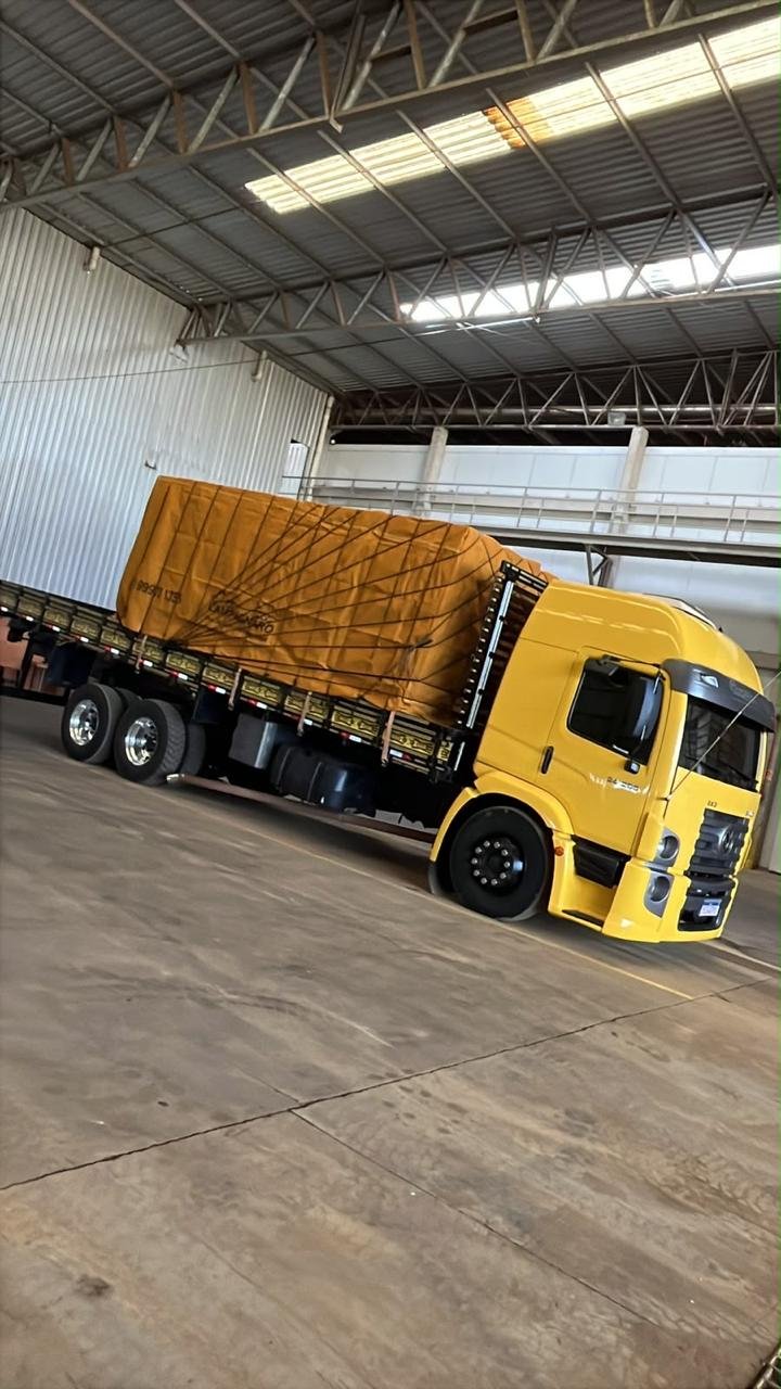 Caminhão da frota JHOW Transportes com carga lonada em pátio coberto